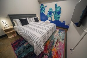 A bedroom with a bed, a nightstand, a wall-mounted TV, and a colorful rug.