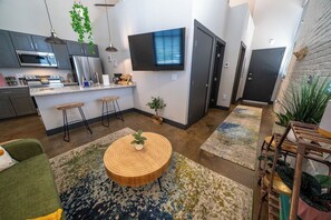 A modern kitchen with stainless steel appliances, a flat-screen TV, and a dining area with a round wooden table.