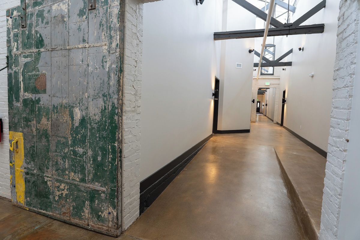A corridor with white brick walls and a concrete floor, leading to a staircase.