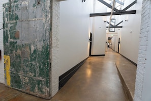 A corridor with white brick walls and a concrete floor, leading to a staircase.