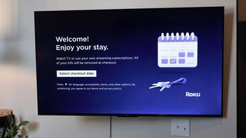 A television screen displaying a welcome message for Roku, with options to select a checkout date and language settings.