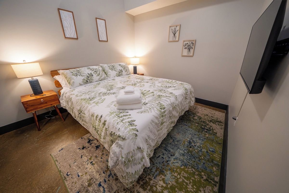 Ein Schlafzimmer mit einem Bett, Nachttischlampen, einem Fernseher und Kunstwerken an den Wänden.