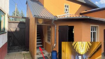 Une maison avec un escalier en bois menant à une porte, un tonneau bleu et un portail en métal.