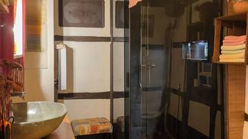 Ein Badezimmer mit Duschkabine aus Glas, einem Holzboden und einer kleinen Ablage.