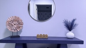 Une table bleu foncé avec un miroir au-dessus, un panier en osier en dessous et un vase avec une plante sur la droite.
