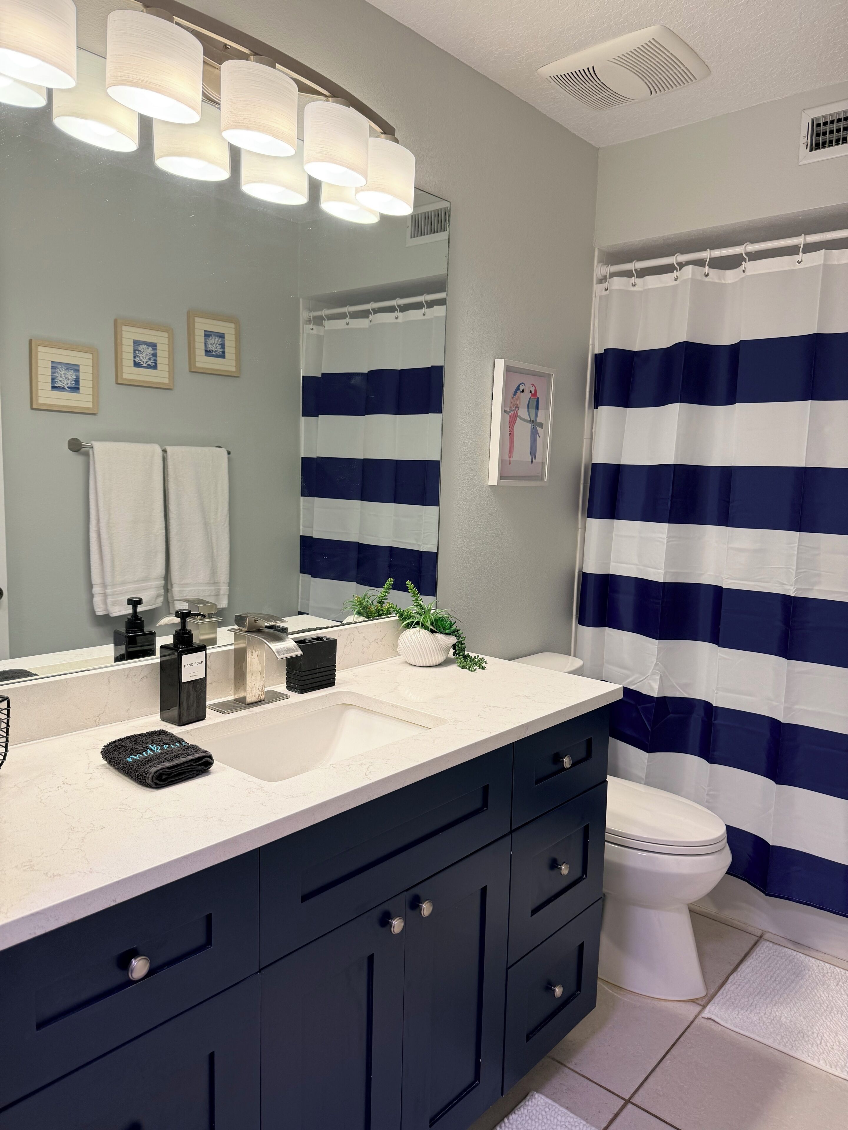 A bathroom with a white sink, dark cabinets, a white toilet, a striped shower curtain, and a mirror with lights.