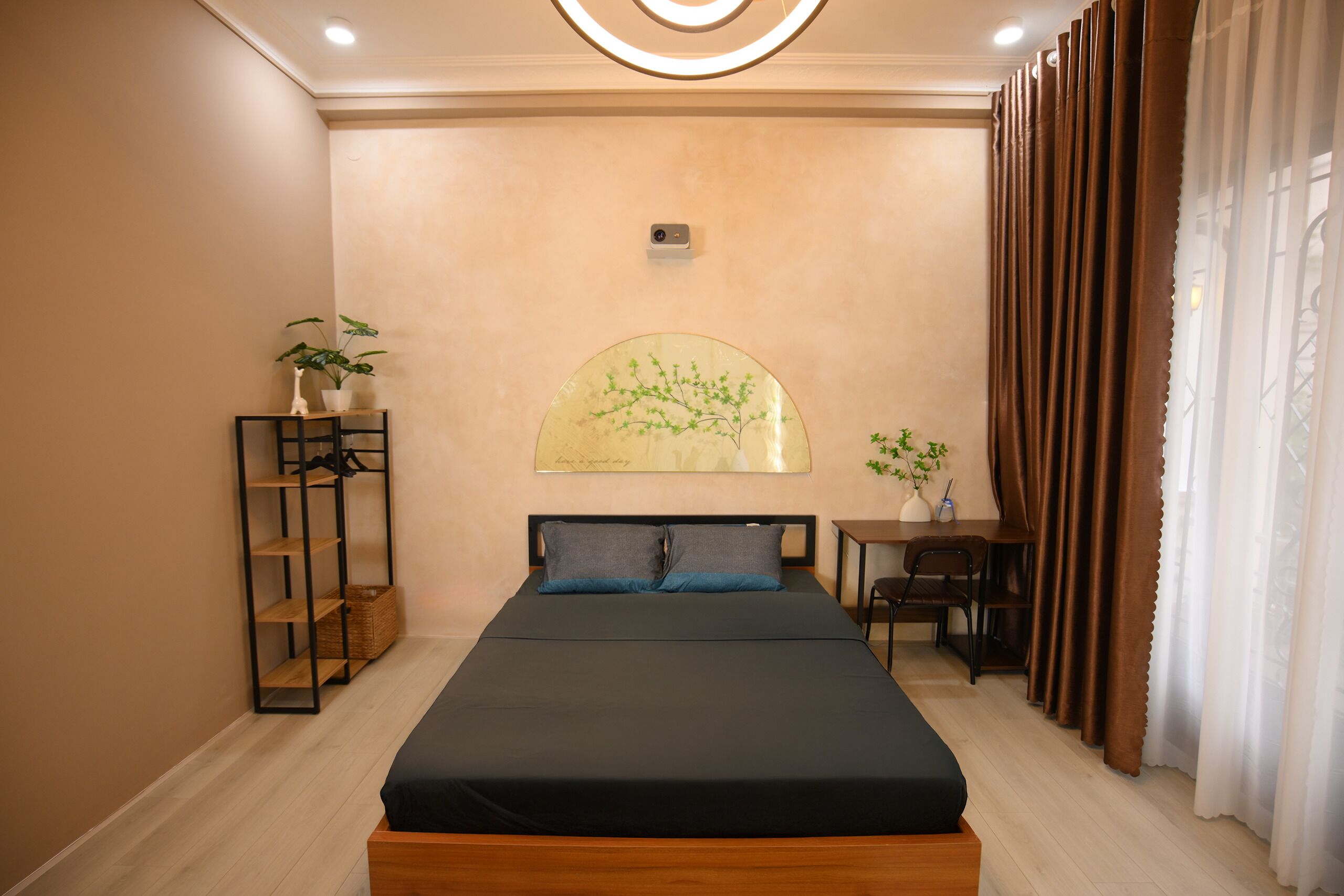 Un dormitorio ordenado con una cama, una mesita, una silla, una estantería con plantas y un cuadro colgado en la pared.