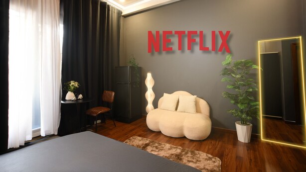 A modern room with a large bed, a seating area with a bean bag, a small table with a plant, and a wall-mounted TV displaying the Netflix logo. - Sora Home - your private sky (Ho Chi Minh City)