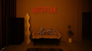 A room with a sofa, a lamp, and a wall-mounted sign that reads "NETFLIX". - Sora Home - your private sky (Ho Chi Minh City)
