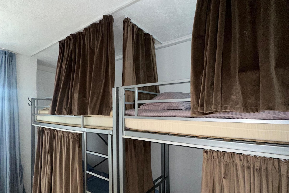 A dormitory room with bunk beds, each covered with brown curtains.
