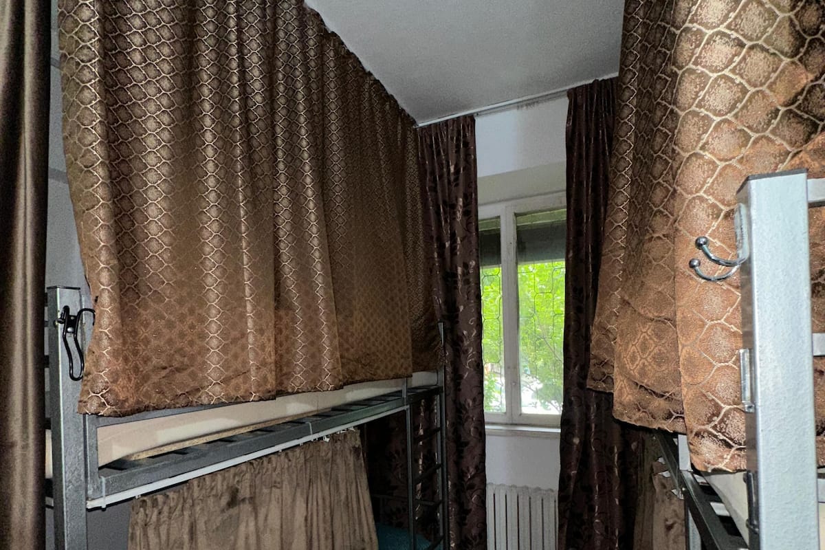A narrow room with bunk beds, brown curtains, a window, and a radiator.
