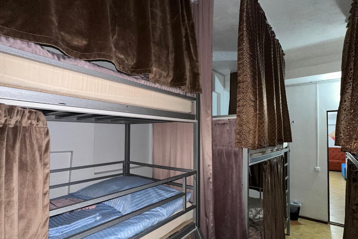 A dormitory room with bunk beds, brown curtains, and a tiled floor.