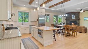 A modern kitchen with white cabinetry, a central island, and a dining area with wooden chairs. - Cozy Lakefront Getaway with Dock, Fire Pit, hot tub & Screened Porch (Catawba)