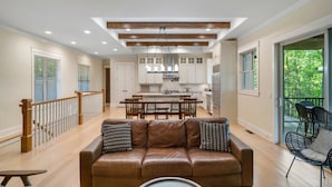 A spacious living area with a leather sofa, wooden ceiling beams, and a view of the kitchen and balcony. - Cozy Lakefront Getaway with Dock, Fire Pit, hot tub & Screened Porch (Catawba)
