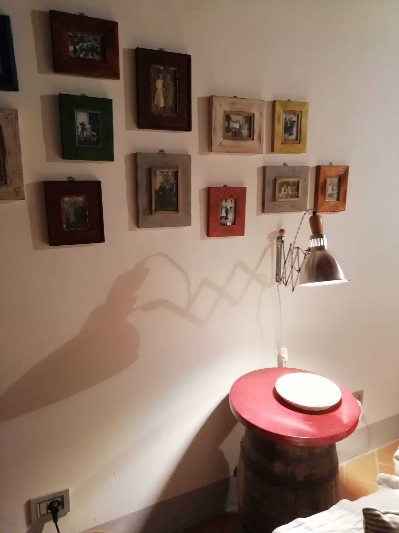 Une pièce dont un mur blanc est orné de plusieurs tableaux encadrés. On y trouve un tonneau rouge avec un couvercle blanc, une lampe en métal et une prise de courant sur le mur.