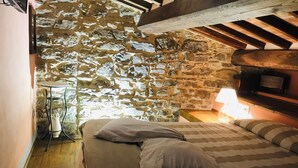 A bedroom with a stone wall, a bed with striped bedding, a bedside lamp, and a wooden floor.