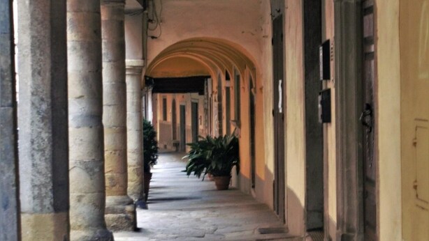 A stone-paved corridor with arches and columns, leading to a building entrance.