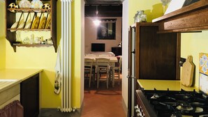 A narrow kitchen with a tiled floor, a stove, a radiator, and a dining area with a table and chairs.