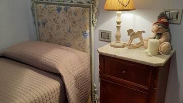 Un dormitorio con cama, una mesita de noche con lámpara, un oso de peluche y un ángel decorativo en la pared.