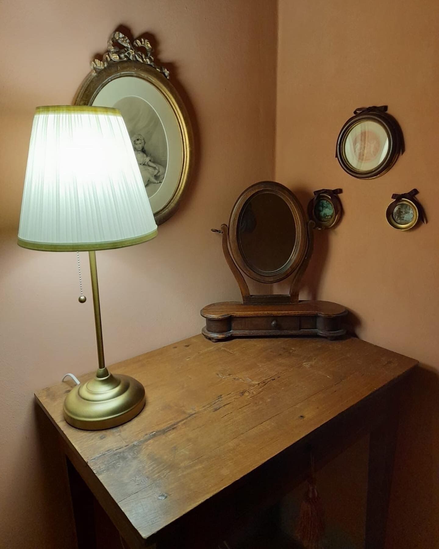 Een houten kaptafel met een messing lamp, een spiegel en twee ingelijste foto's aan de muur.
