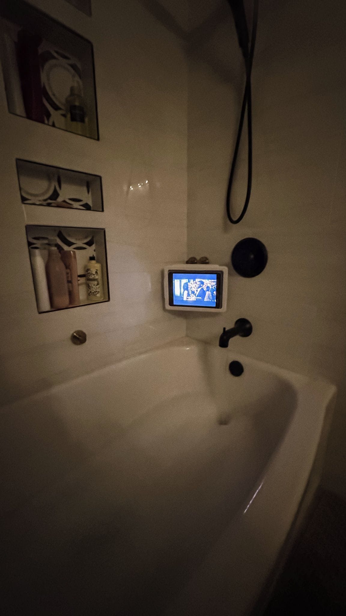 A bathroom with a white sink, a small screen mounted on the wall, and a towel rack with towels.