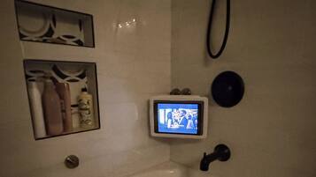 A bathroom with a white sink, a small screen mounted on the wall, and a towel rack with towels.
