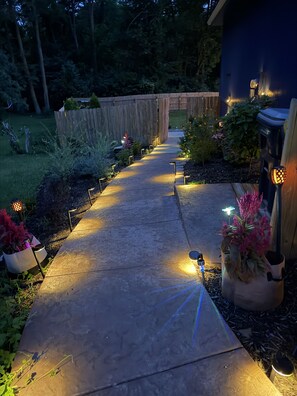 A well-lit pathway with potted plants and outdoor lighting fixtures. - Heated Swim Spa + Outdoor Movie Theater, Private Resort (Kansas City)