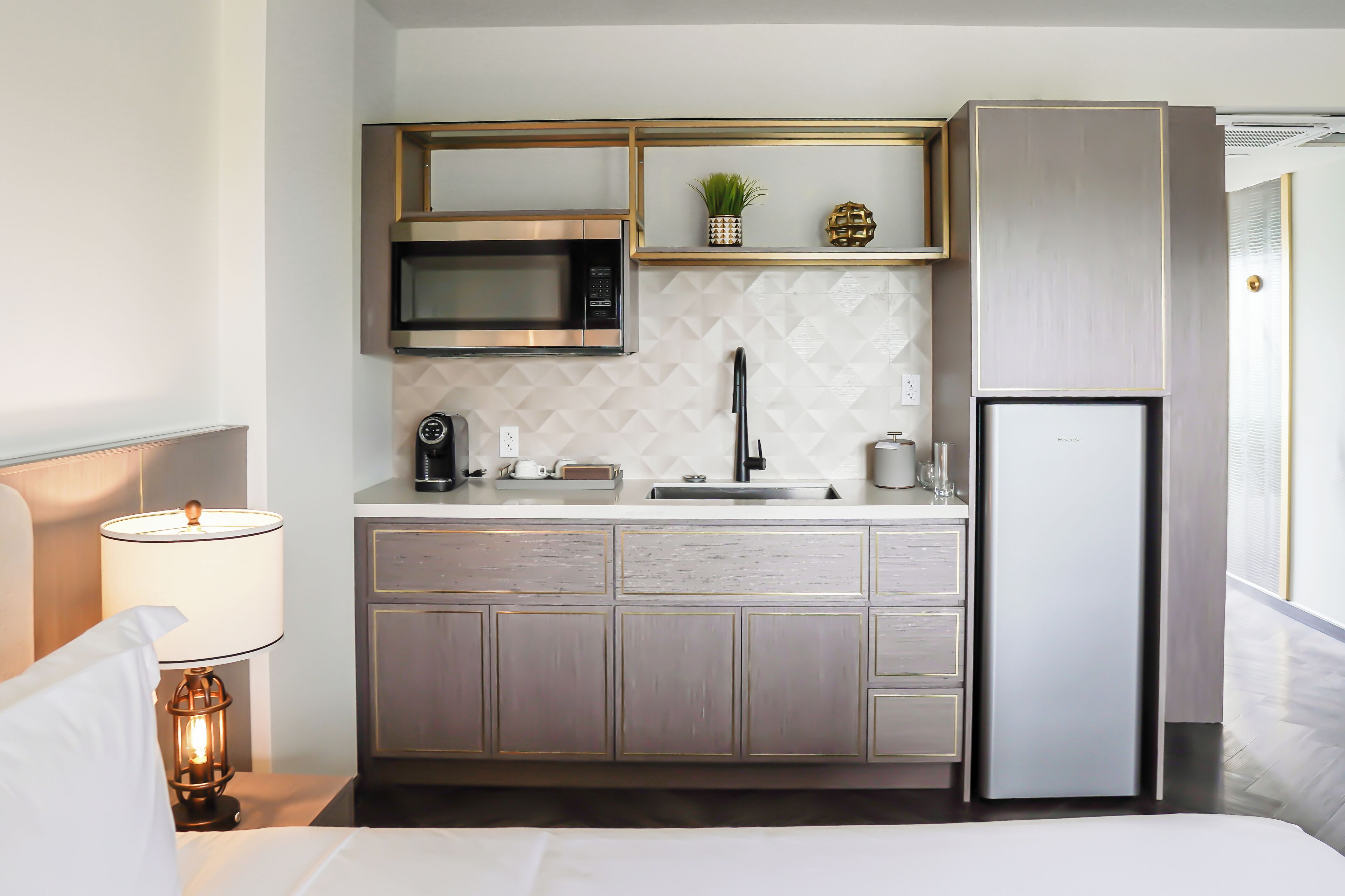 A compact kitchen with a microwave, sink, and refrigerator, featuring a geometric backsplash and wooden cabinets.