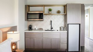 Eine kompakte Küche mit Mikrowelle, Spüle und Kühlschrank, mit einem geometrischen Rücksprung und Holzschränken.
