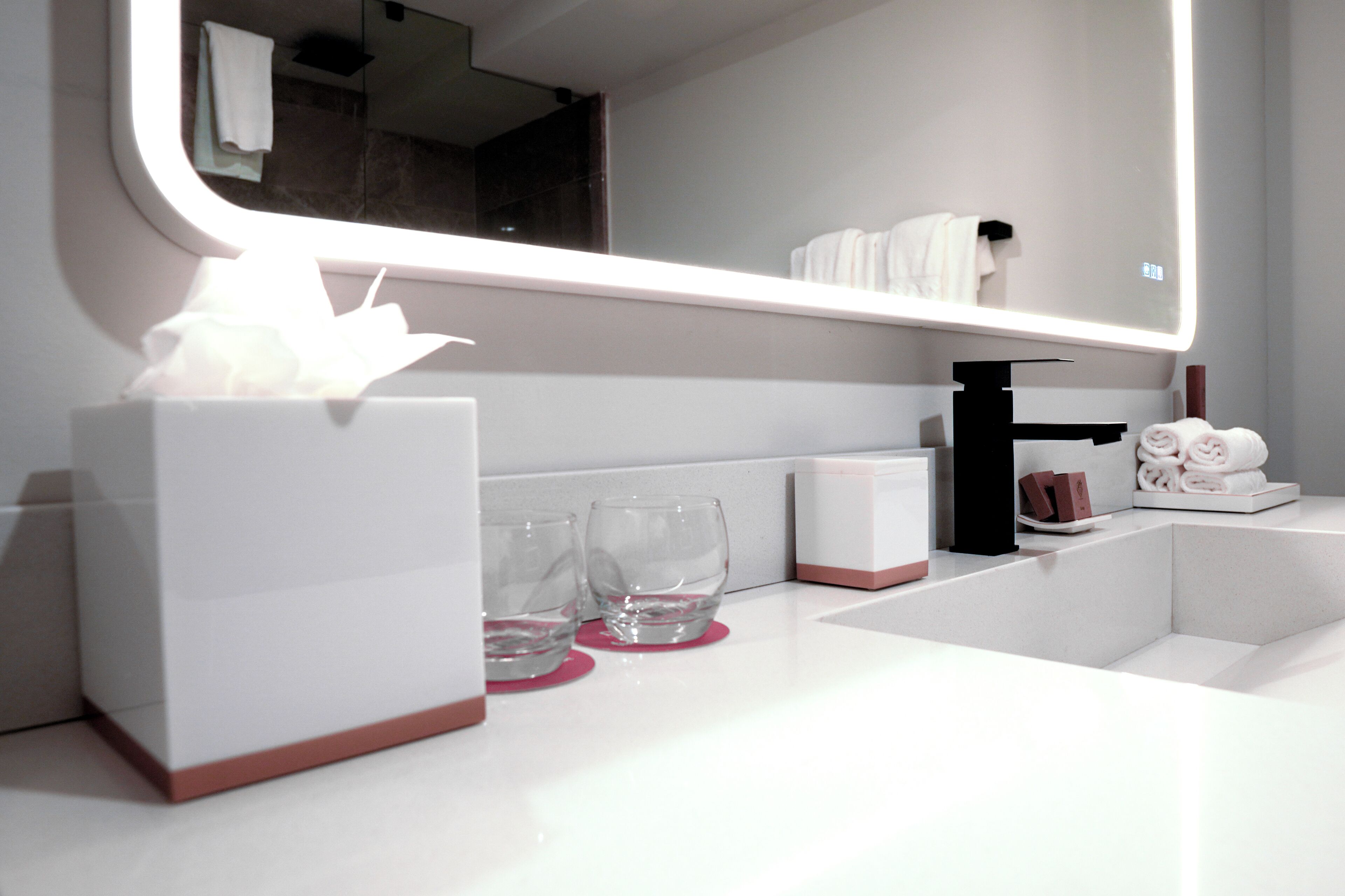 A modern bathroom with a white sink, a mirror, and a tissue box.