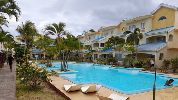 Une piscine avec des chaises longues, des palmiers et un bâtiment aux toits bleus.