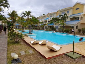 A swimming pool with lounge chairs, palm trees, and a building with blue roofs.