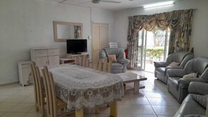 Un salon comprenant une table à manger, des canapés, un téléviseur et un ventilateur de plafond.