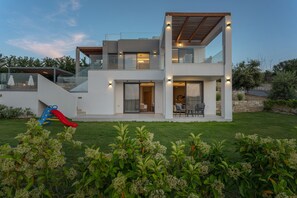 A modern two-story house with a slide in the yard, large windows, and a stone wall.