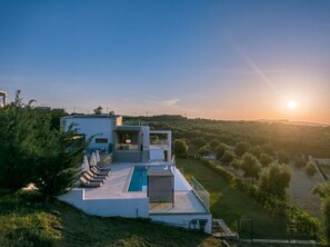 A modern villa with a swimming pool, outdoor seating, and a view of the countryside.