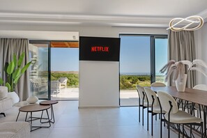 Una sala de estar moderna con un televisor de pantalla plana grande, un comedor y un balcón con vista al mar.