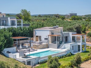Una villa moderna con piscina, mobiliario exterior y vistas del paisaje circundante.