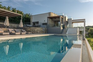 Un área de piscina moderna con una piscina cristalina, sillas de descanso y un muro de piedra.