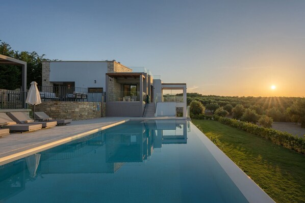 A modern house with a swimming pool, outdoor seating, and a view of the sunset.