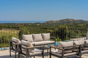 A balcony with outdoor furniture, a pool, and a scenic view of hills and coastline.