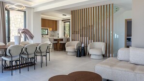A modern living room with a sofa, chairs, a coffee table, and a kitchen area in the background. - Skyline Villa II, By Hellocrete (Aggeliana)