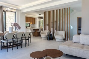A modern living room with a sofa, chairs, a coffee table, and a kitchen area in the background.