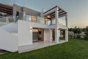 A modern two-story house with a glass balcony, a stone wall, and a well-maintained lawn. - Skyline Villa II, By Hellocrete (Aggeliana)