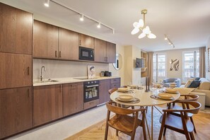 A modern kitchen with wooden cabinets, a microwave, an oven, and a dining area with a table set for four. - Sublim Apartement in the Center of Paris/le Marais (Paris)