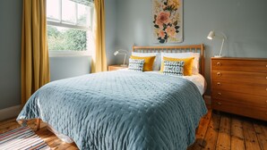 A bedroom with a bed, wooden dresser, nightstands, and a window with curtains. - Cleve Cottage by inspirestays.com - a cottage that sleeps 4 guests in 2 bedrooms (Lewes)