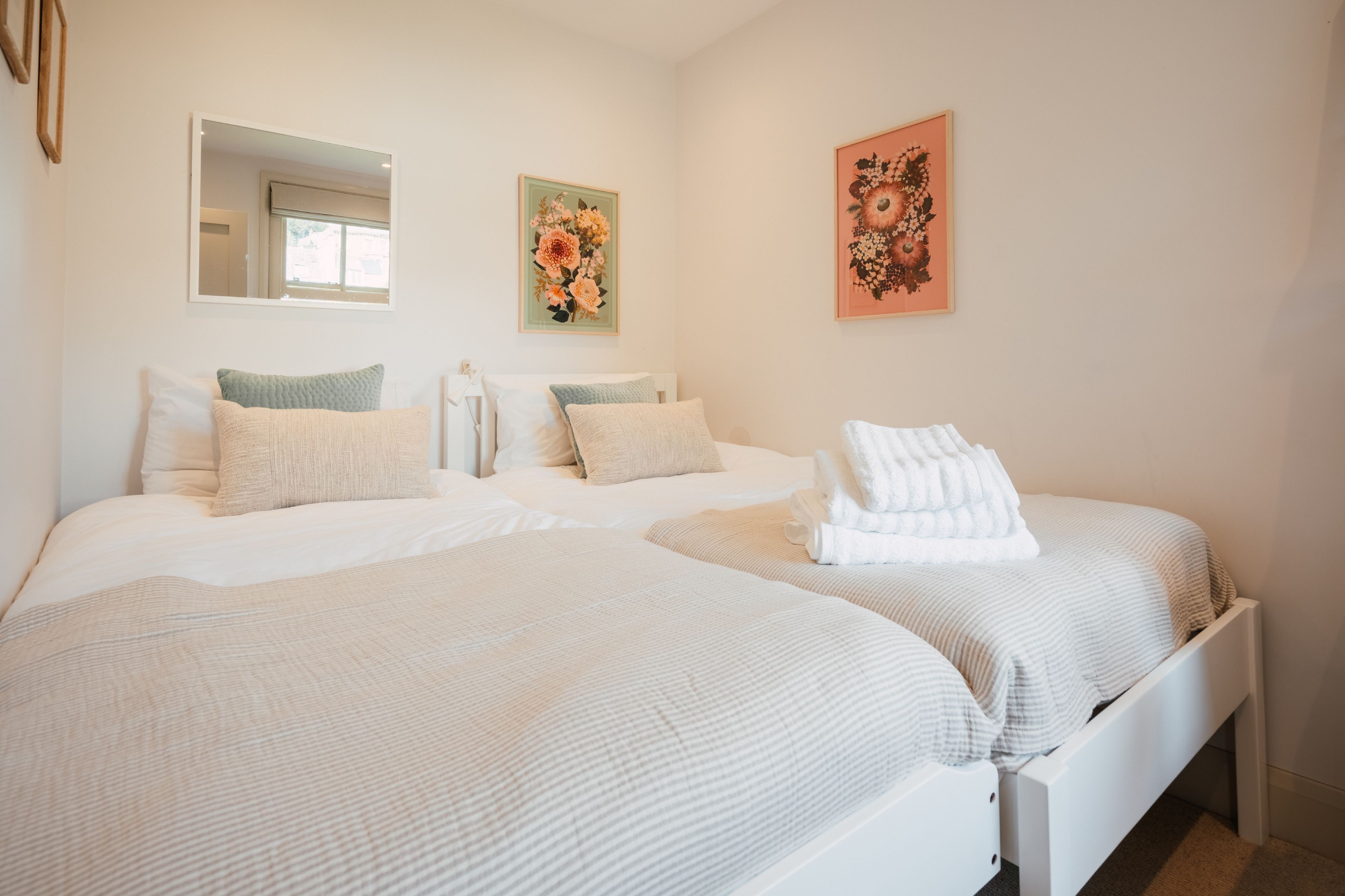 Een hotelkamer met twee bedden, een grote spiegel en twee bloemige wanddecoraties.