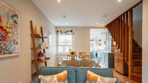 A modern living room with a blue sofa, wooden shelves, and a dining area with a table and chairs. - Cleve Cottage by inspirestays.com - a cottage that sleeps 4 guests in 2 bedrooms (Lewes)