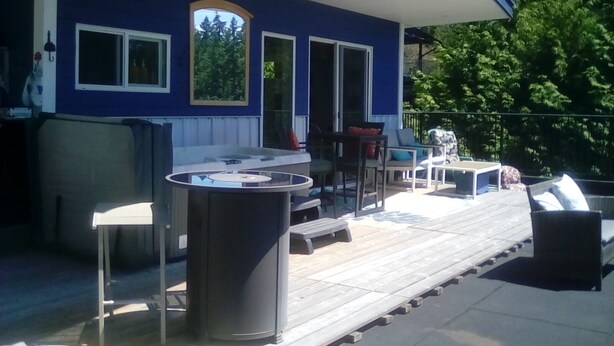 A covered outdoor deck with a barbecue grill, seating area, and a view of the surrounding greenery. - Cloud 9 roof top studio in Maderia Park is waiting for your enjoyment. (Madeira Park)