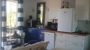 A compact kitchen with a sink, microwave, and coffee maker. There is a white refrigerator and a blue cabinet. A wicker chair is visible in the foreground. - Cloud 9 roof top studio in Maderia Park is waiting for your enjoyment. (Madeira Park)
