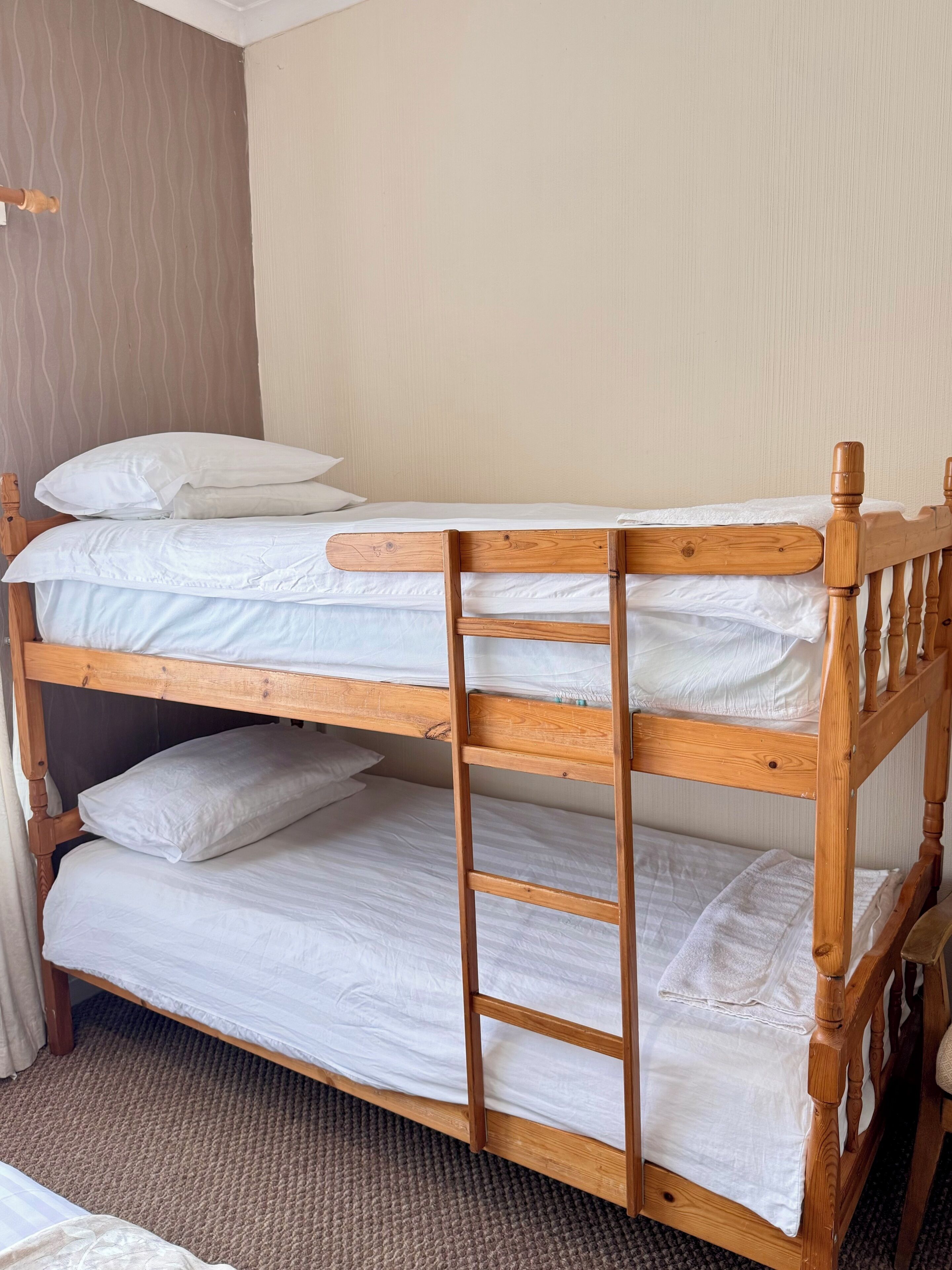 A bunk bed with wooden headboards and footboards, white bedding, and a ladder for access.